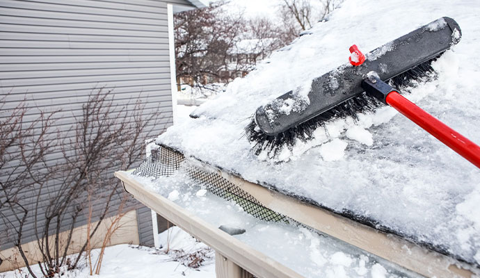 Rake tool clearing accumulated snow and ice buildup from a roof edge