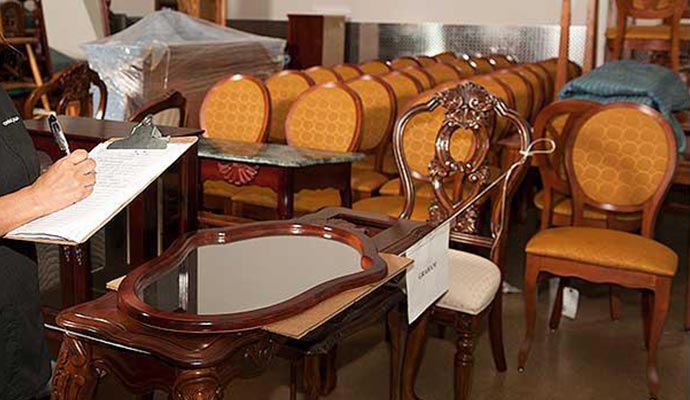 Person inspecting and documenting furniture in a room with chairs and tables