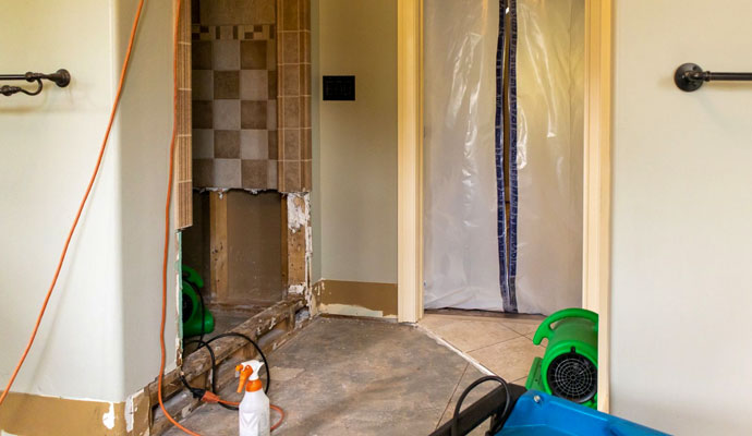 Commercial air movers drying walls and floors in a water-damaged bathroom