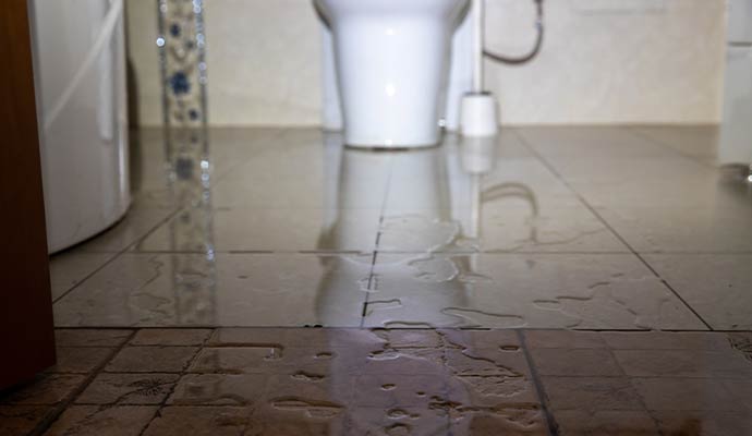 Water flooding a tiled bathroom floor from a toilet overflow