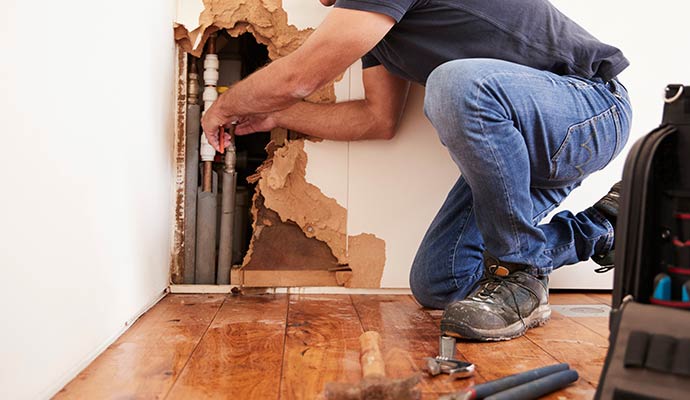 Plumber repairing a burst water pipe inside a wall.